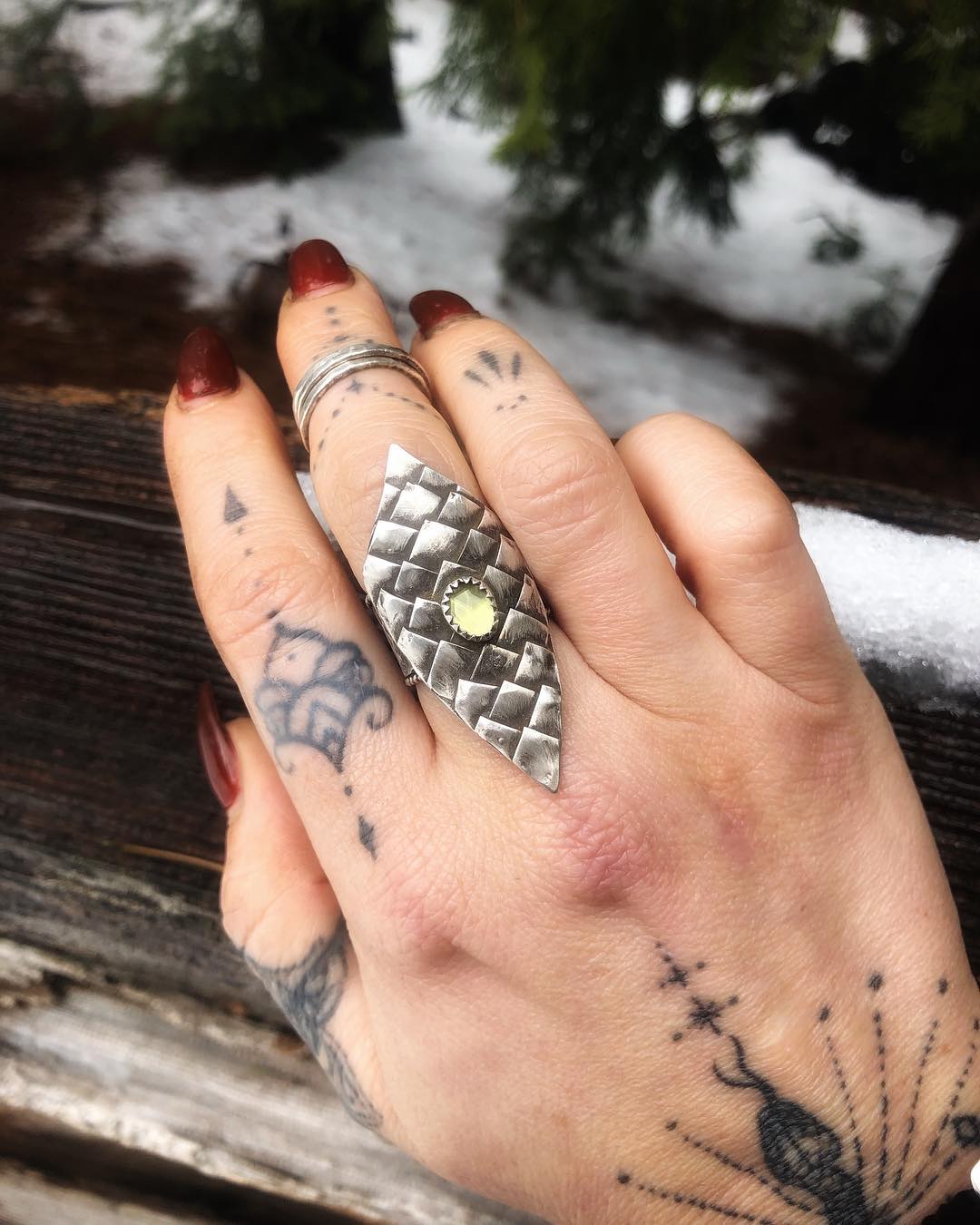 Jenna's tattooed hand wearing a hand-forged scale ring, held over snow