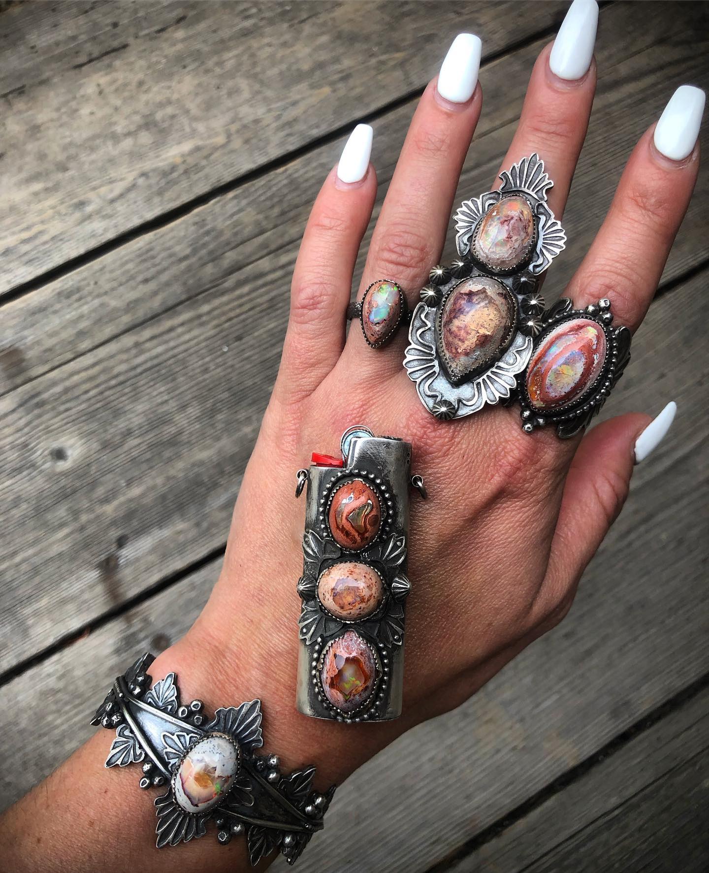Jenna's whole tattooed hand on weathered wood, wearing a cluster of fire opal rings, a FireKeeper lighter case and an opal cuff