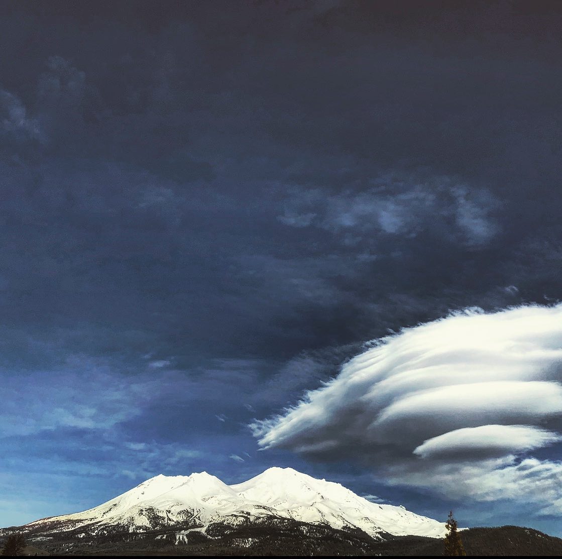 Mount Shasta under a stacked lenticular cloud, snow on the peak, forest at its foot