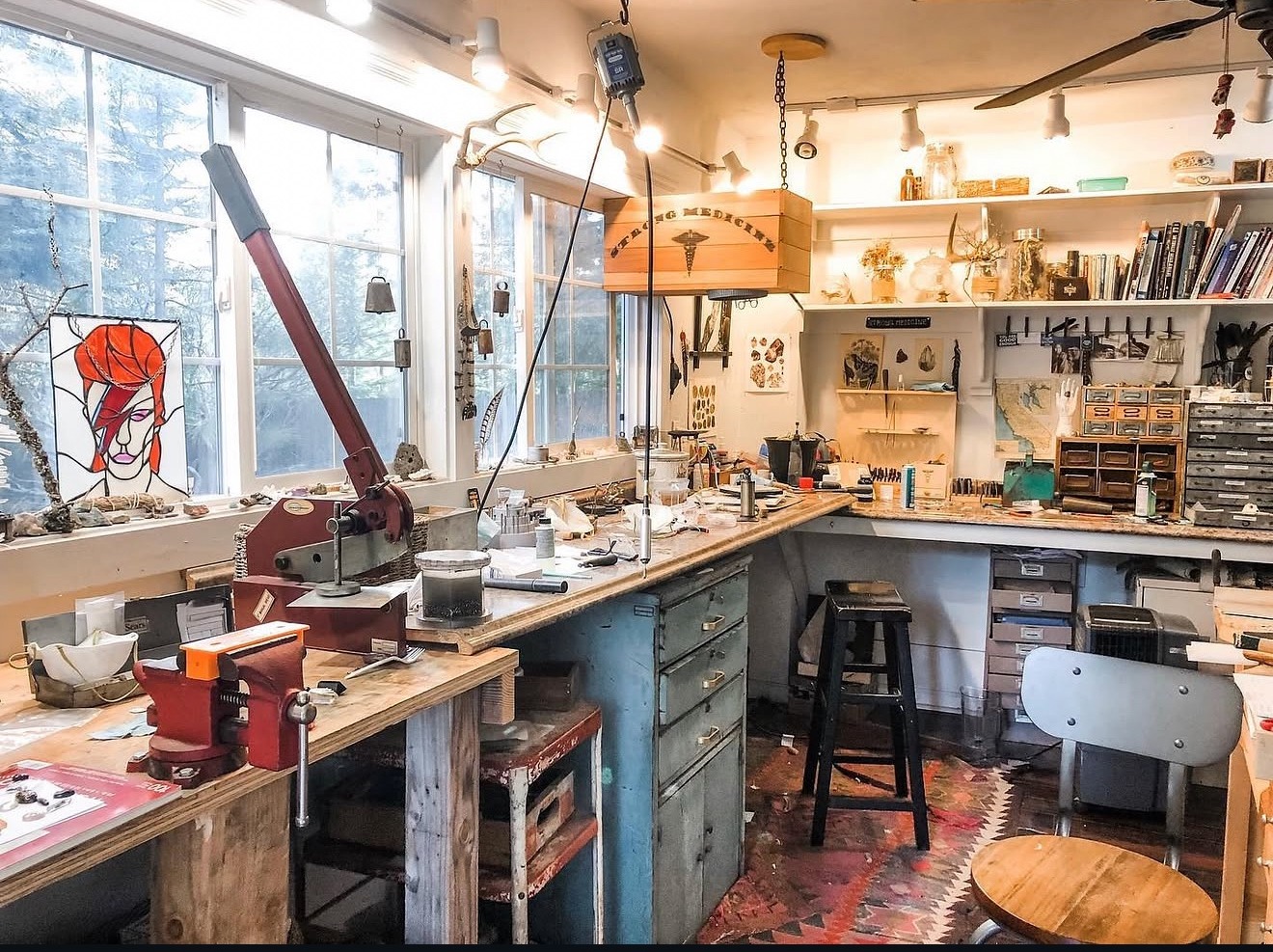 The full studio — benches, tools, drawers and tall windows looking onto the trees
